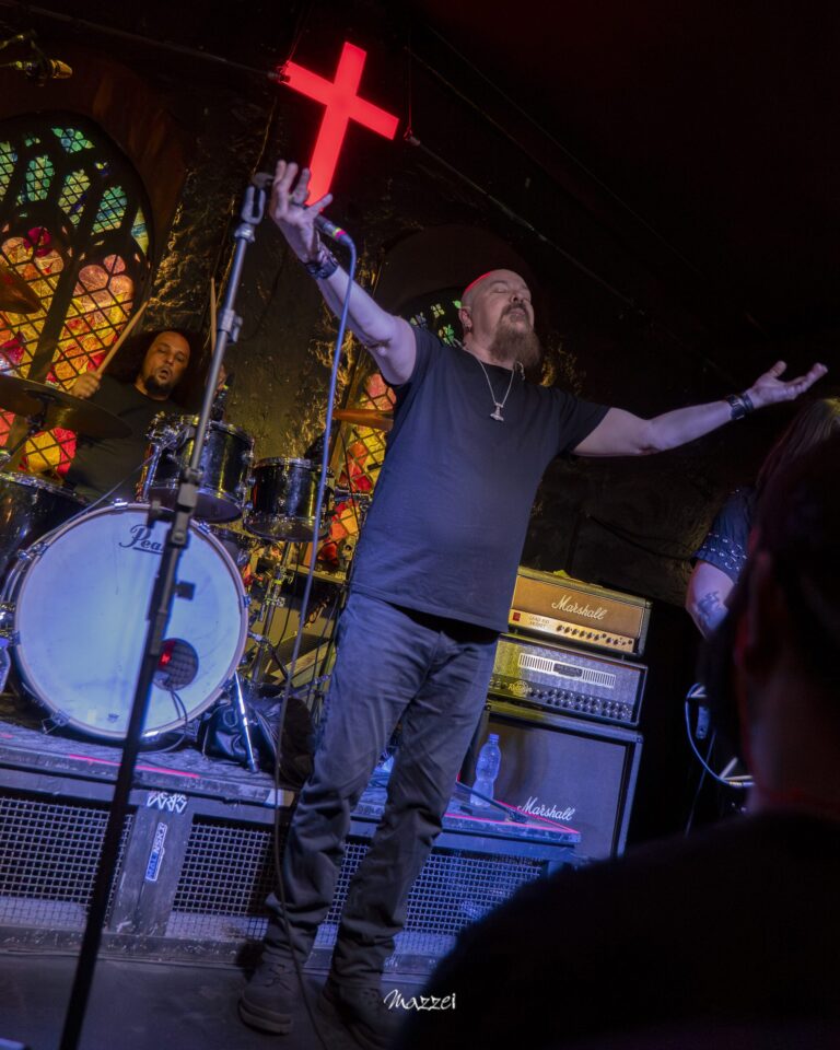 Robert Lowe with arms open under a red neon cross at La Iglesia, São Paulo