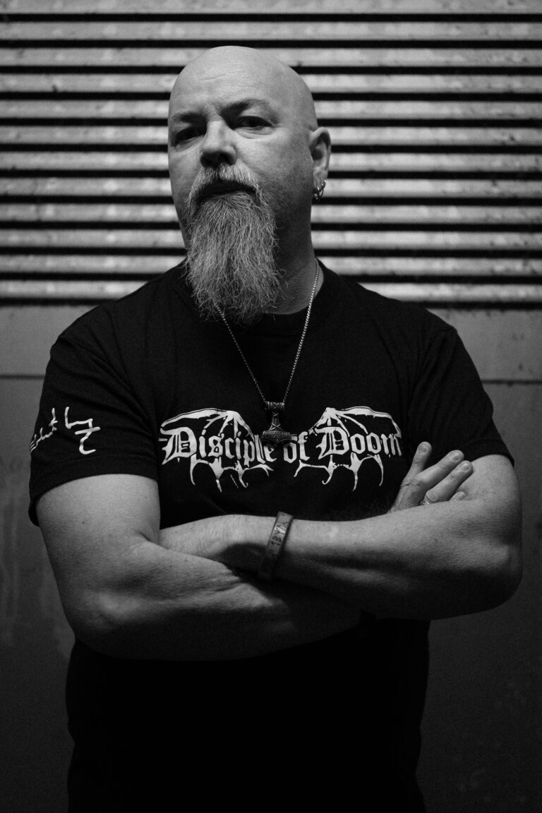 Robert Lowe, arms crossed, wearing a Disciple of Doom shirt