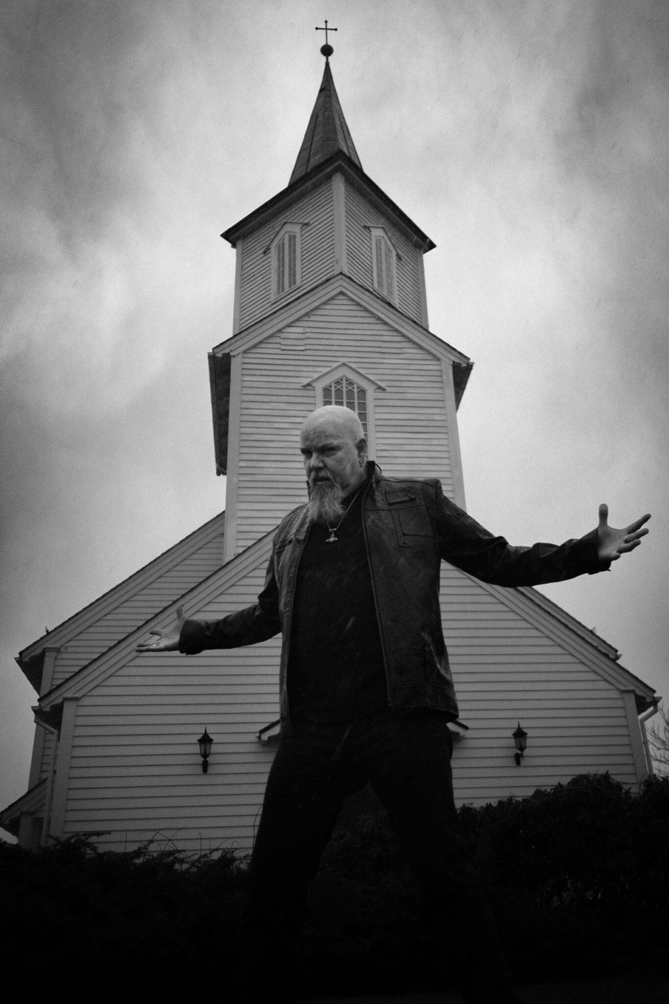 Robert Lowe with arms open in front of a white wooden church